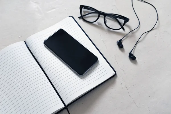 hafif bir arka plan üzerinde siyah bir açık not etmek üstünde bir defter gözlük siyah jant ve siyah kablolu müzik kulaklık ile yanındaki siyah bir smartphone olduğunu; bir yazıt için boş bir alan
