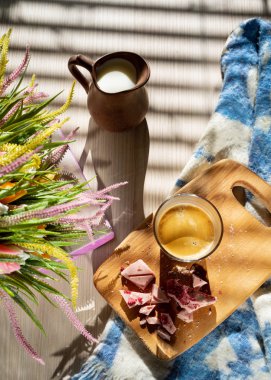 yatakta, cam bir fincan siyah kahve, bir süt sürahi, bir kara tahta ve kır çiçekleri, düşük ışık, dikey çerçeve bir buket üzerinde ufalanmış pembe çikolata