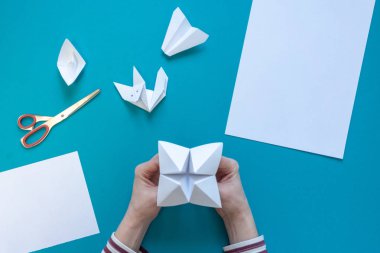 Genç bir kızın elleri origami kağıt sanat yapmak, mavi bir arka plan temiz beyaz kağıt, makas, uçak, tekne ve tilki, üst görünümü