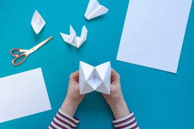 Genç bir kızın elleri origami kağıt sanat yapmak, mavi bir arka plan temiz beyaz kağıt, makas, uçak, tekne ve tilki, üst görünümü