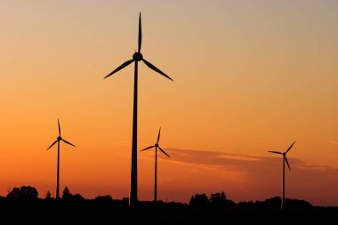 Four windturbines against dramatic sunset producing environment friendly energy clipart