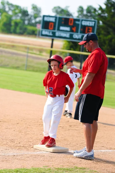 Baseball coach giving instruction to player at first base during a game.