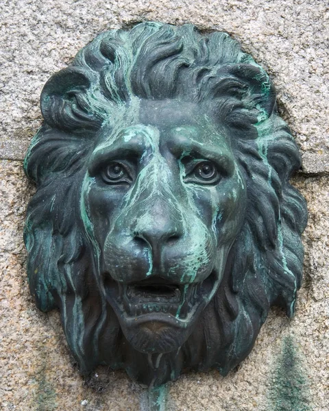 Antique bronze lion mask fixed to a granite block wall
