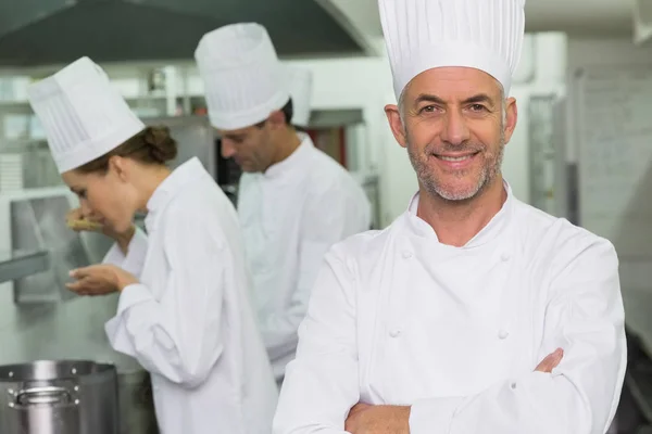 Happy chef looking at camera with team working behind in a commercial kitchen