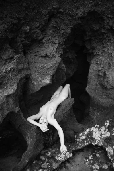 Young nude Caucasian woman lying on rocks in cave.