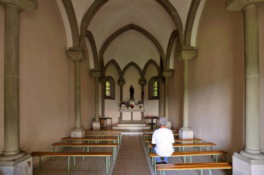 Inside a small chapel with a single worshipper sitting on a bench. clipart