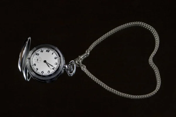 Silver pocket watch and a chain from watch in the form of heart on a black background