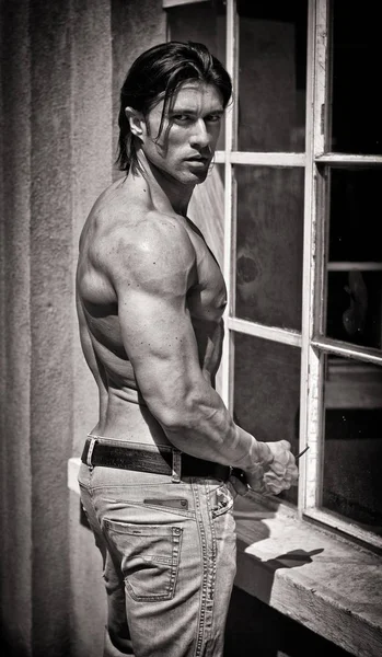 Profile of muscular young bodybuilder shirtless outdoors in jeans, black and white shot
