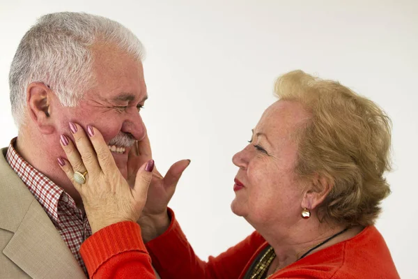A senior couple laughing each other and and lady holding his face.