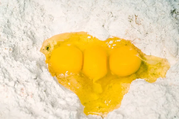 Three egg yolks sitting in a hole in some baking flour