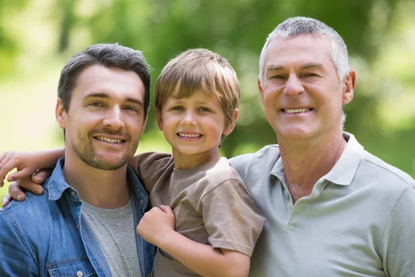 Grandfather father and son smiling against blurred background at the park