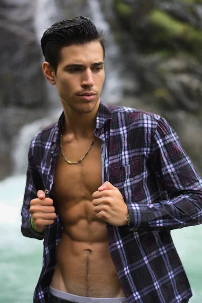 英俊的年轻男子与敞领衬衫 山瀑布附近撕开矫健的身形 — 图库照片