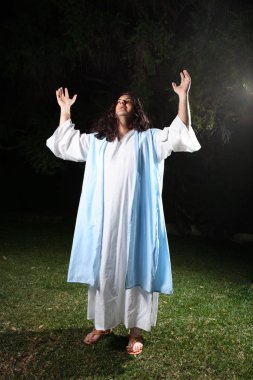 Man wearing white robe and over cloak standing outdoors bathed in light praising and glorifying God.   From (Psalm. 29:2) Give unto the Lord the glory due unto his name  worship the Lord in the beauty of holiness clipart