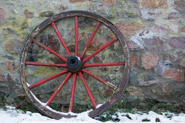 Old wooden wagon wheel on a stone wall in winter