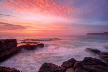 Glorious summer sunrise skies over North Avoca rockshelf and a soft sea spray mist and motion in the waves.  NSW Australia clipart