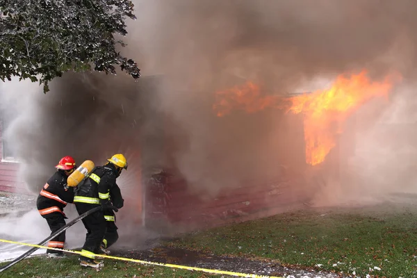 Tres Bomberos Durante Intenso Entrenamiento Con Una Casa Llamas Fondo — Foto de Stock