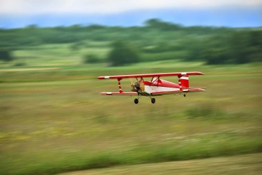 Red and white radio controlled aircraft with methanol engine flying over grassy field. The image shows motion blur. clipart