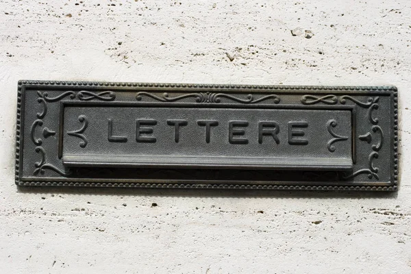 An iron vintage mailbox on gray wall, with the letters written in Italian
