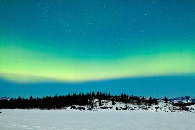 Spectacular display of intense green Northern Lights or Aurora borealis or polar lights over snowy northern winter landscape clipart
