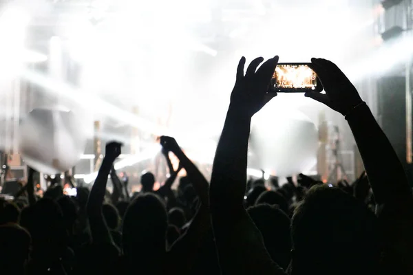 Silhouette of hands recording videos at music concert. Pop music concert with lights, smoke and lots of people