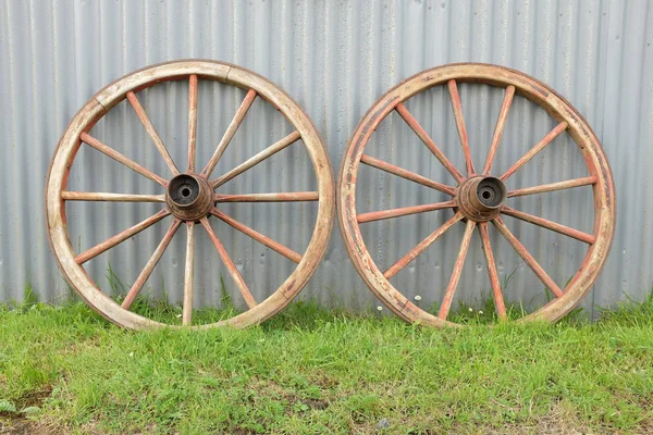 绿草通向一对木制的古董车车轮靠在金属墙上 — 图库照片