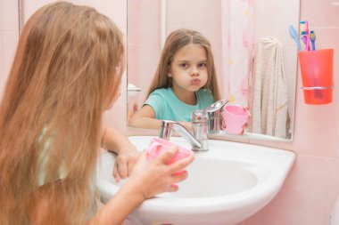 Six year old girl washes and brushes his teeth in the bathroom clipart