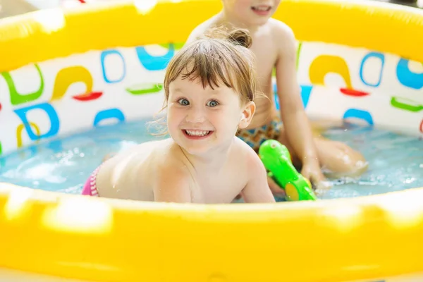 Little girl bathes in yellow Inflatable Swimming Paddling Pool outdoors in hot summer day. Kids in Swim Pool