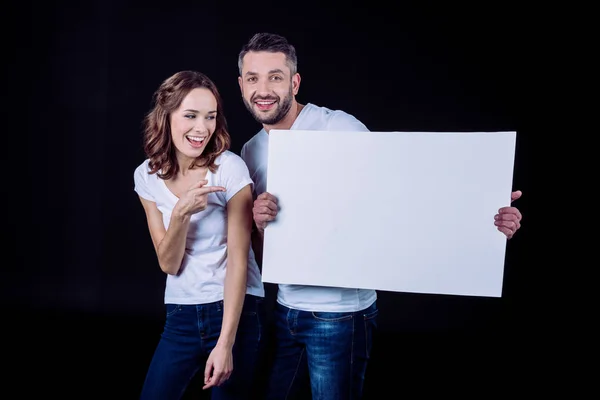 Pareja Sonriente Camisetas Blancas Sosteniendo Tarjeta Blanca Blanco Mujer Señalando — Foto de Stock