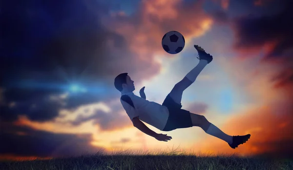足球运动员踢反对绿草深蓝色和橙色的天空下的白色 — 图库照片