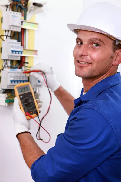 Smiling electrician using multimeter on electric meter