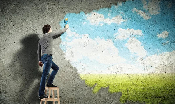 若い男が壁に曇った青空を描画 — ストック写真