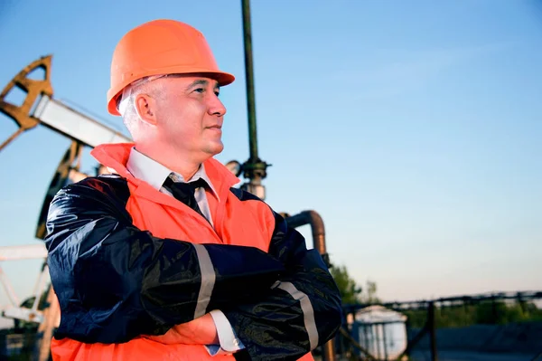石油工人的橙色制服和头盔上的背景泵杰克和蓝蓝的天空 — 图库照片