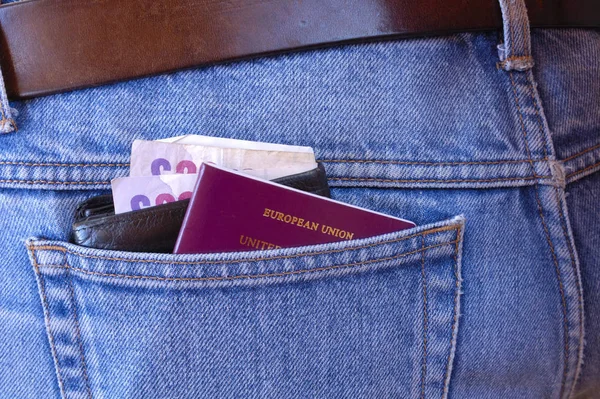 A passport, and a wallet, containing several 20 notes, poke out of the rear pocket of someone's jeans. A temptation for a pickpocket.