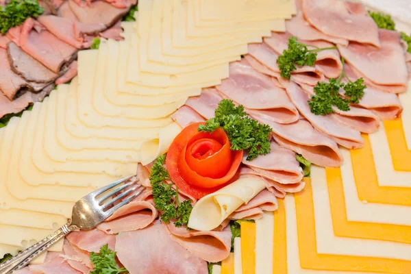 Party tray of assorted meats and cheeses with  flower made of tomato in the middle.