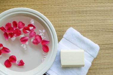 Minimalistic spa setting with floating rose petals, fluffy white towel, and all-natural soap bar. clipart