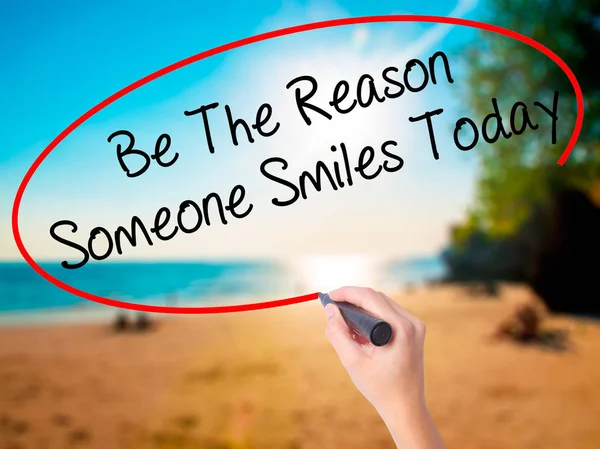 Women Hand writing Be The Reason Someone Smiles Today  with black marker on visual screen. Isolated on beach. Business, technology, internet concept. Stock Photo