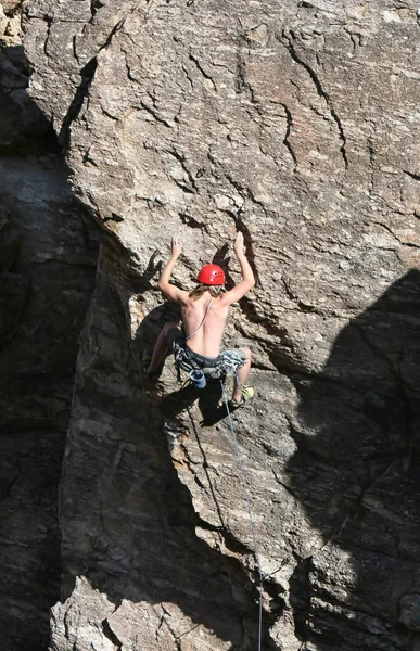 A rock climber works his way up a rock face protected by a rope clipped into bolts. He is wearing a helmet and quickdraws dangle from his harness. The route is in the desert southwest United States. Mt Lemmon, Arizona.