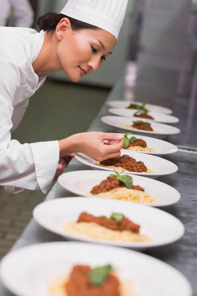 商業キッチンでスパゲッティ料理にバジルの葉を置く幸せなシェフ — ストック写真