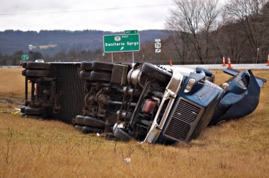 A tractor trailer on its side in the median after a roll over accident. clipart