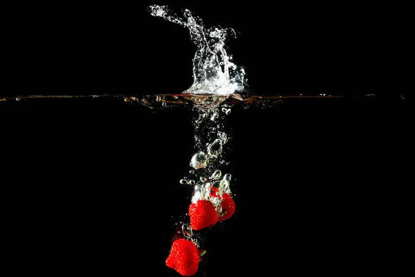 黒の背景にはねかける水の着色された赤パプリカ — ストック写真