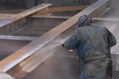 sandblaster working at industrial premises of factory clipart