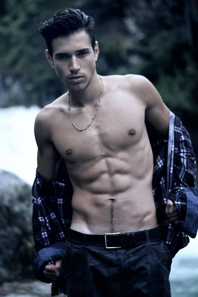 英俊的年轻男子与敞领衬衫 山瀑布附近撕开矫健的身形 — 图库照片
