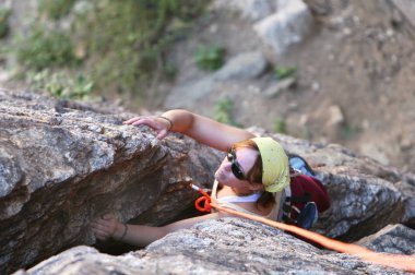 A young woman climbs a crack in the rock. She is secured by top rope belay. clipart