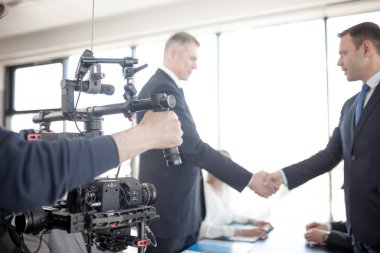 Videographer using steadycam, making video of business people shaking hands clipart