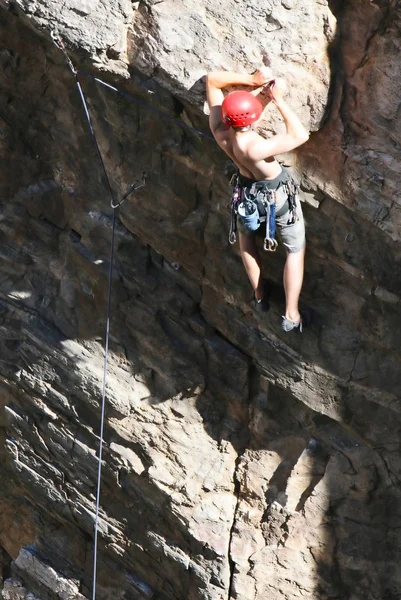 A rock climber works his way up a rock face protected by a rope clipped into bolts. He is wearing a helmet and quickdraws dangle from his harness. The route is in the desert southwest United States. Mt Lemmon, Arizona.