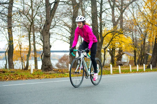 Young Woman in Bright Pink Jacket Riding Road Bicycle in the Park in the Cold Autumn Day. Healthy Lifestyle Concept.