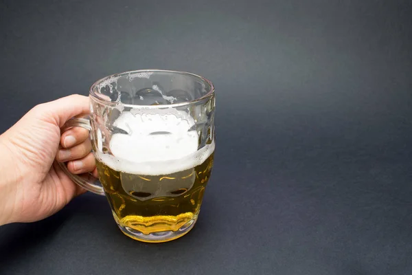 Hand holds golden pint of beer in a dark background