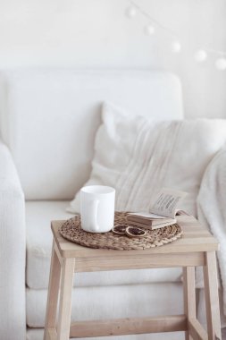 Still life interior details, cup of coffee and a book near white cozy chair clipart