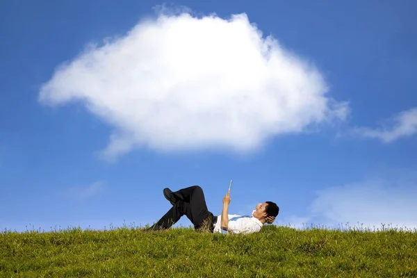 云背景和快乐的商人在绿草上与平板电脑工作 — 图库照片