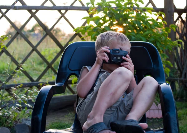 カメラを持つ子供は暖かい夏の夜に黒いプラスチック製のアームチェアに座っています — ストック写真